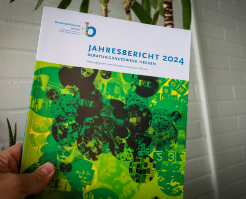 Bild einer Hand, die den Jahresbericht 2024 des "Beratungsnetzwerk Hessen - Gemeinsam für Demokratie und gegen Rechtsextremismus" hält.