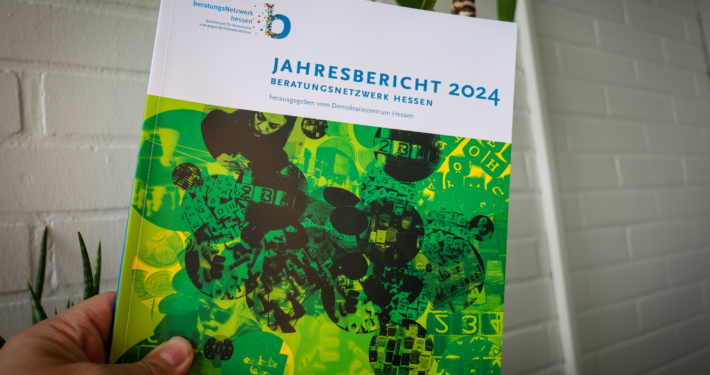 Bild einer Hand, die den Jahresbericht 2024 des "Beratungsnetzwerk Hessen - Gemeinsam für Demokratie und gegen Rechtsextremismus" hält.